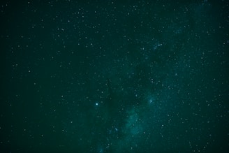 A vast, dark night sky is filled with countless small stars, creating a cosmic spectacle. The Milky Way galaxy is prominently visible, stretching across the scene with subtle gradients of light and dark, adding to the celestial beauty.