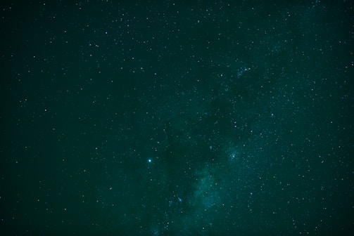 A vast, dark night sky is filled with countless small stars, creating a cosmic spectacle. The Milky Way galaxy is prominently visible, stretching across the scene with subtle gradients of light and dark, adding to the celestial beauty.