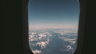 Snow-capped mountains viewed from an airplane window on a clear day.