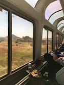 First-class train interior with plush seats and large windows overlooking rolling countryside.