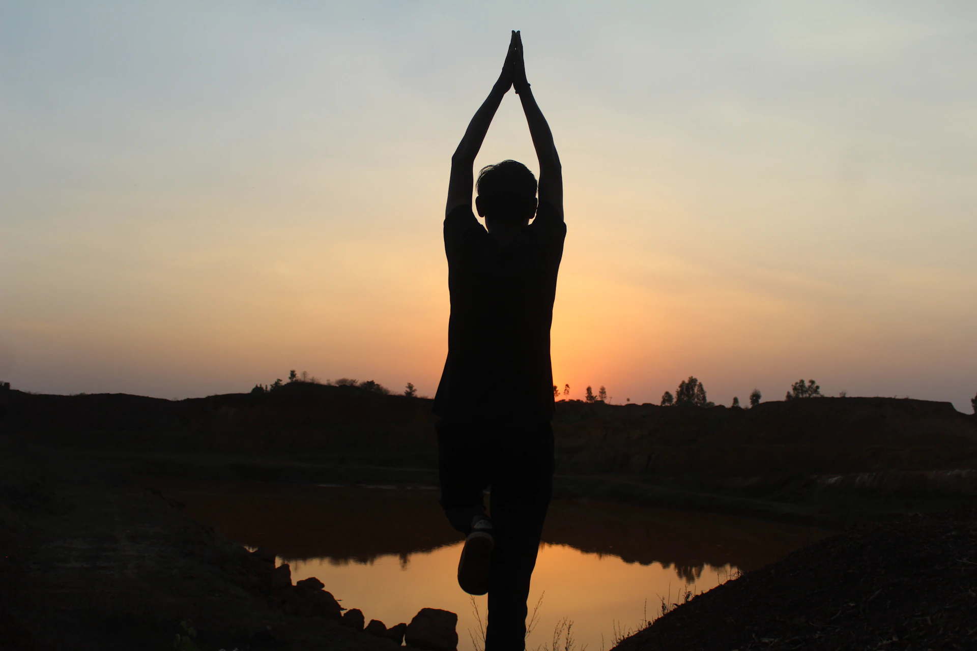 A peaceful yoga session at sunrise with a silhouette of a person in meditation pose against a calm, colorful sky.
