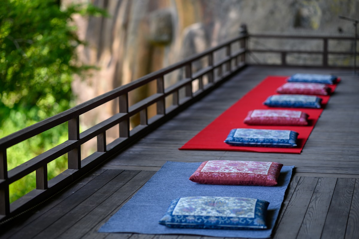 Row of meditation cushions arranged on a wooden deck before practice, soft daylight