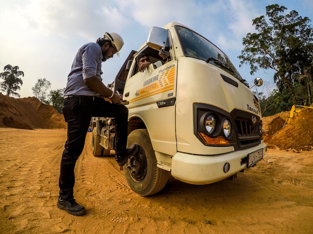 man standing in front of white drop-side truck during daytime