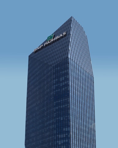 A modern skyscraper with a glass facade and the logo of BNP Paribas displayed prominently at the top against a clear blue sky. The building is characterized by its rectangular shape with vertical lines, creating a sleek and professional appearance.
