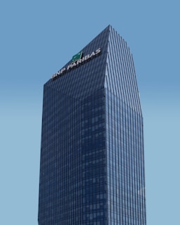 A modern skyscraper with a glass facade and the logo of BNP Paribas displayed prominently at the top against a clear blue sky. The building is characterized by its rectangular shape with vertical lines, creating a sleek and professional appearance.