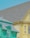 The image features two adjacent houses with distinct and vibrant colors. The house on the left is painted a bright teal color with intricate trim details and a gray shingled roof, while the house on the right is a pastel yellow with a matching roof. Both houses exhibit architectural charm, suggesting a residential neighborhood.