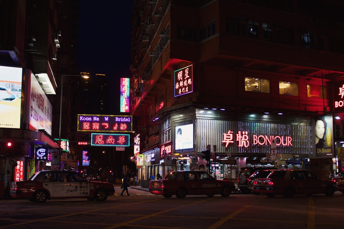 Vehicles on road with people walking near buildings during nighttime in Hong Kong
