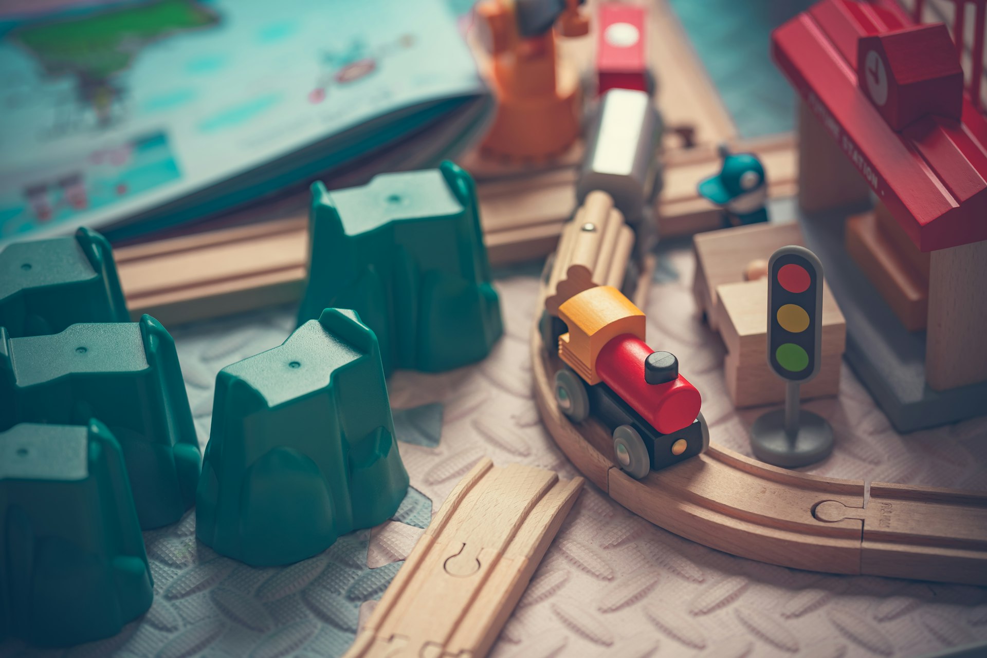 A wooden toy train rounding a curve of wooden track beside a little red station