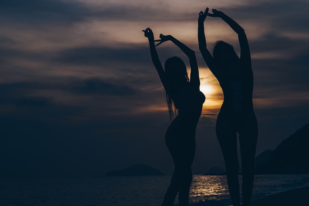 silhouette of women lifting hands in front of sea