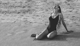 A sunlit beach scene showcasing a model in a sleek black one-piece swimwear, embodying effortless elegance.