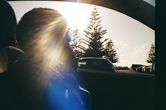 A friendly technician applying window tint film to a car under bright sunlight.