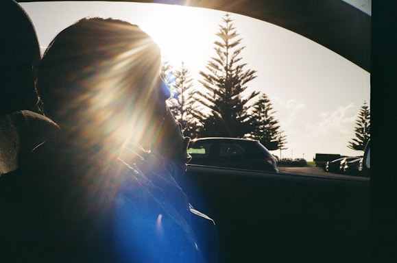 A friendly technician applying window tint film to a car under bright sunlight.