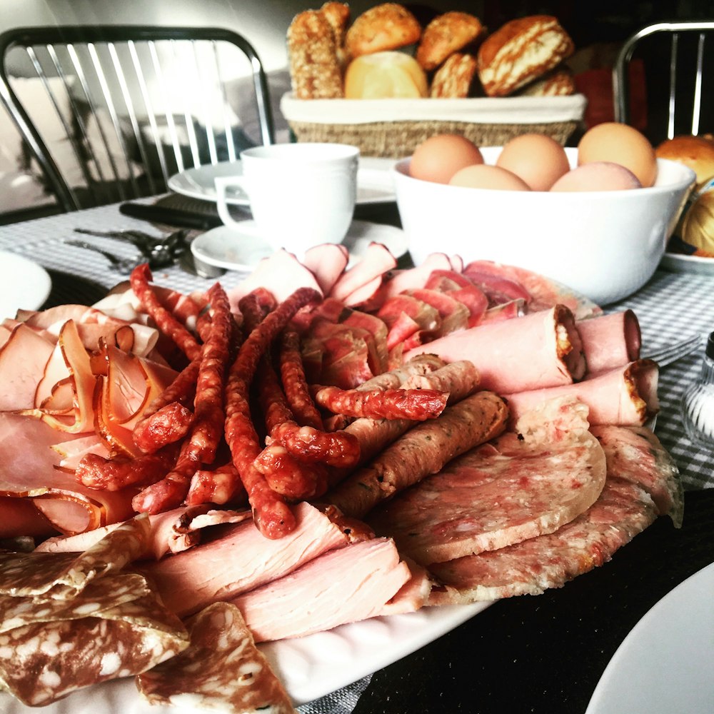 sausages near sliced ham beside chicken eggs in bowl on table