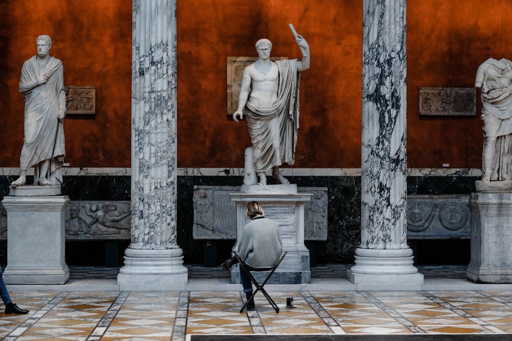 person sitting on chair with cross legs near three men statue