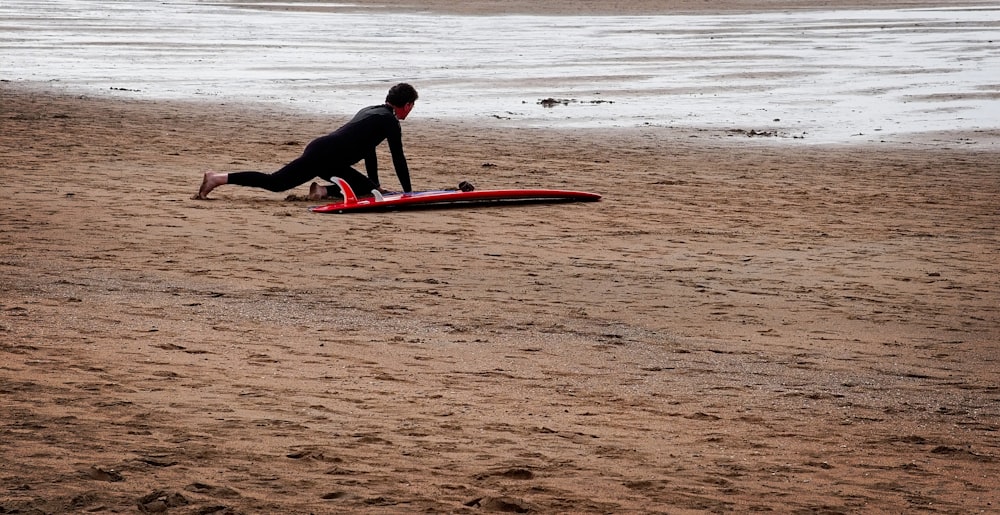 man in black wet suit on red surfboard on shore