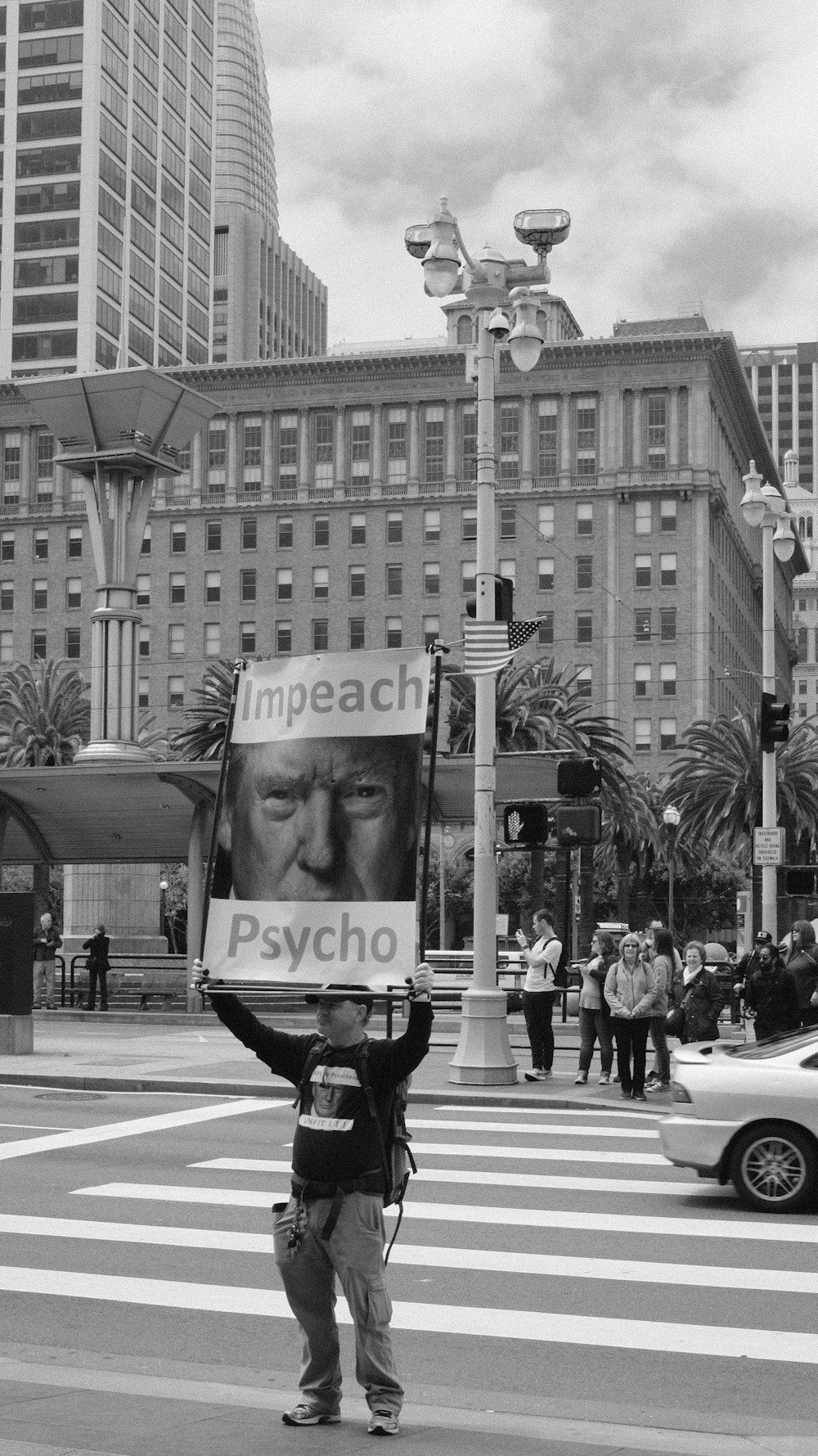 greyscale photography of man standing on road holding psycho banner