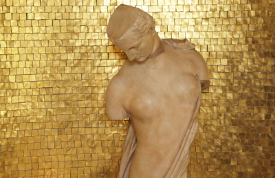 Soft pastel background with delicate gold accents framing a vintage Greek statue of Aphrodite.