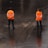 Two individuals dressed in bright orange jackets with reflective stripes stand on a wet, dark surface. The jackets have 'Protección Civil' written on the back. They appear to be observing or monitoring the surrounding area.