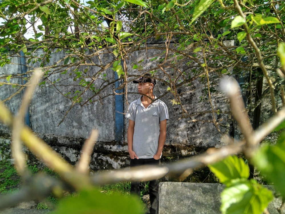 man in white polo shirt standing under tree