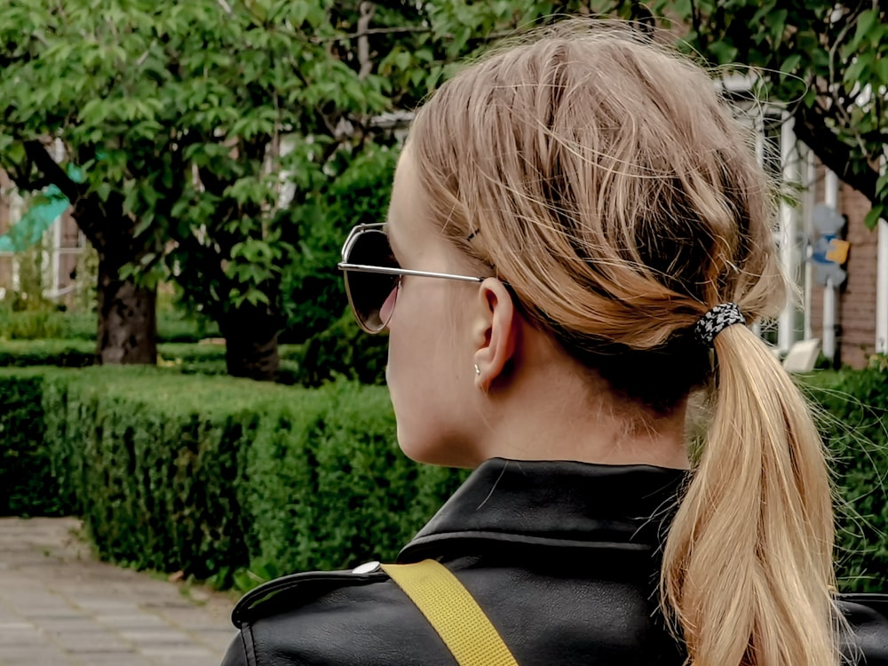 woman in black leather jacket wearing sunglasses standing near bush