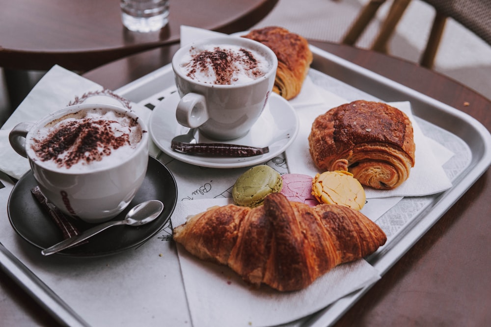 two cups of coffee, two cinnamon rolls and croissant on serving tray