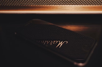 A sleek black smartphone displaying the Roam Romance app with gold accents glowing softly.