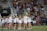 A large group of people, mainly young girls, are gathered on a sports field. Most are wearing matching outfits consisting of white shirts and dark shorts. The event appears to be in a stadium setting with many spectators seated in the background, indicating it may be a sporting or celebratory event.