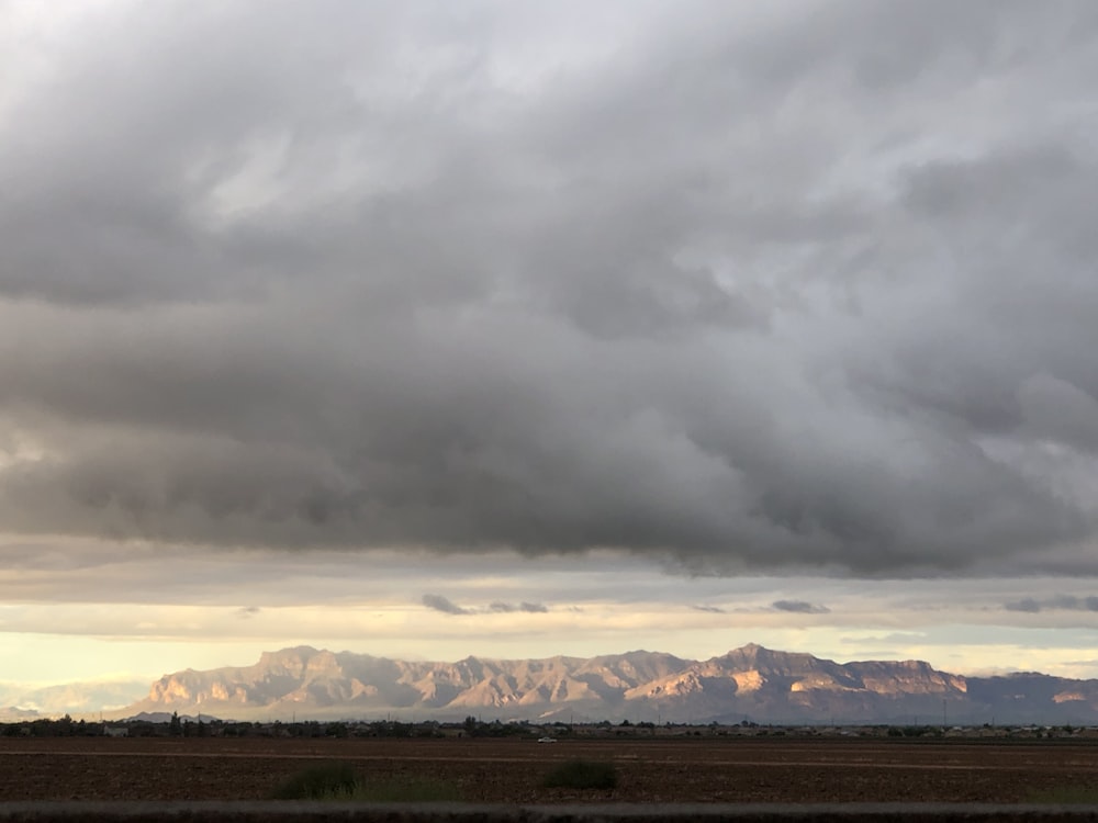 a cloudy sky over a field with mountains in the distance