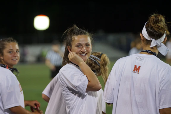A warm, inviting photo of diverse young athletes smiling together on a sunny sports field.