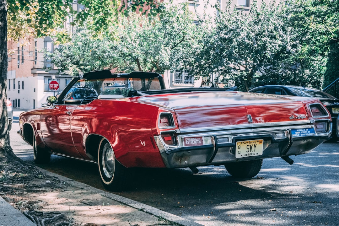 red convertible coupe parkes on sidewalk besie tree