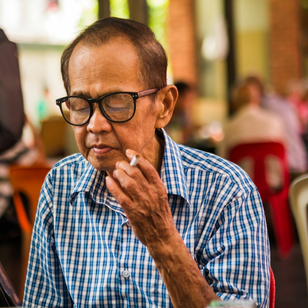 man wearing eyeglasses holding cigarette looking down