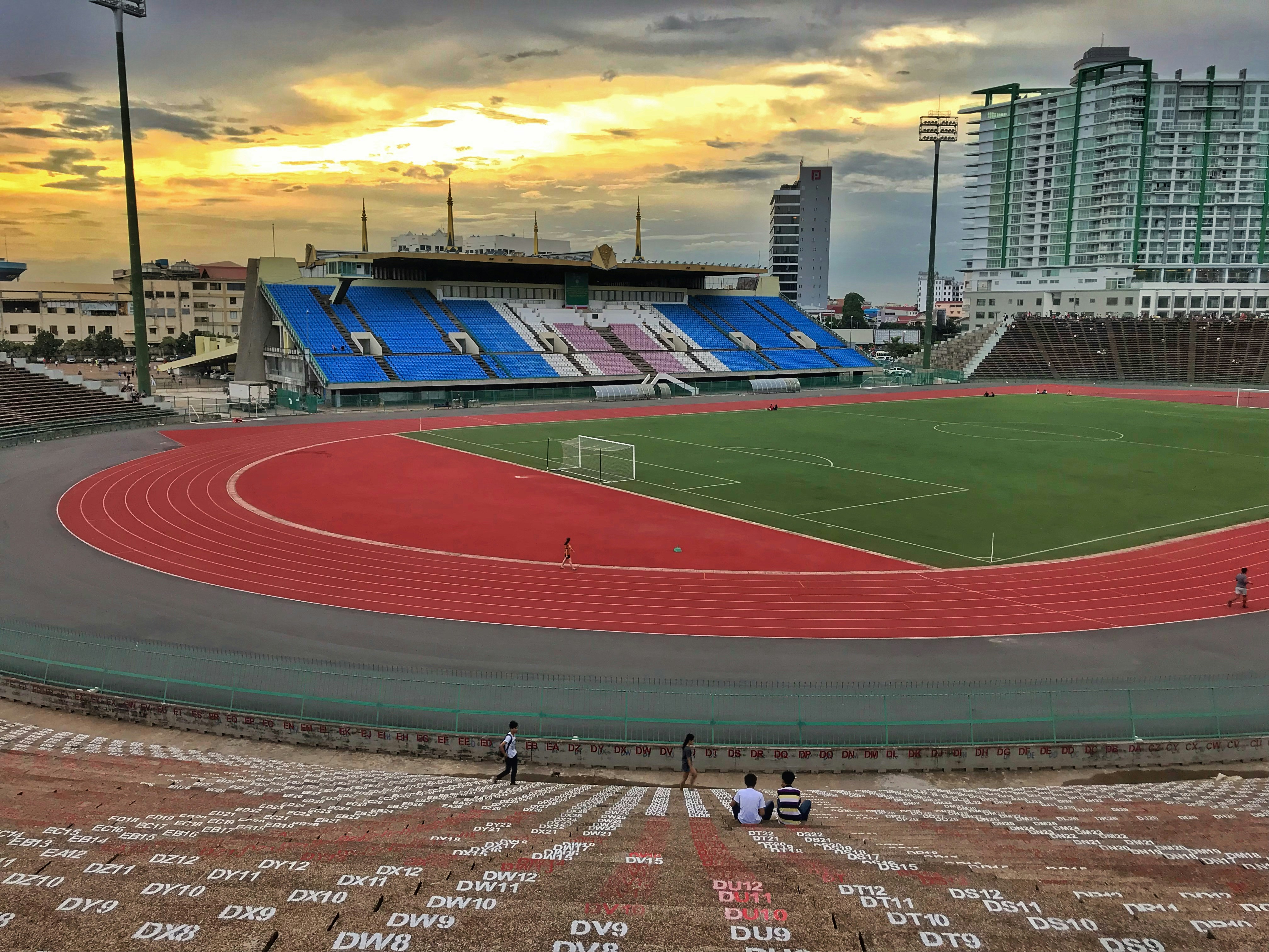 Athletes running on outdoor track at sunset with dramatic sky background