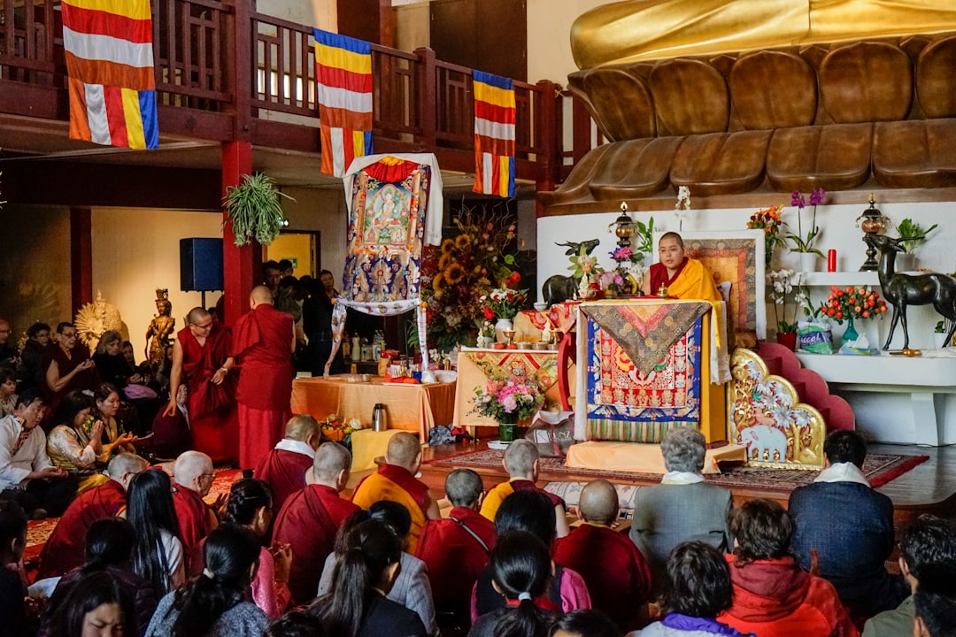 Dalai Lama sitting near table surrounded with people watching