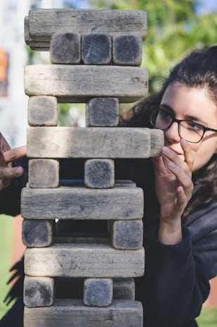 Close-up of hands setting up a giant Jenga game on a wooden picnic table outdoors.