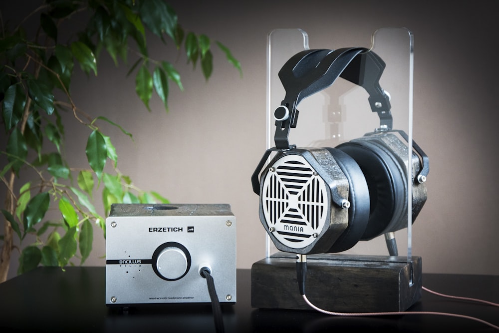 black and gray corded headphones near gray speaker on table