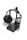 A pair of large, black headphones with cushioned ear pads is resting on a minimalist wooden headphone stand. The stand is constructed from dark-stained wood and has a metal frame that holds the headphones in place. A thin audio cable is connected to the headphones and extends towards the bottom of the image.