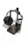 A pair of large, black headphones with cushioned ear pads is resting on a minimalist wooden headphone stand. The stand is constructed from dark-stained wood and has a metal frame that holds the headphones in place. A thin audio cable is connected to the headphones and extends towards the bottom of the image.
