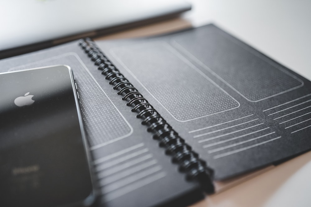 schwarzes iPhone auf schwarzem Spiral-Notebook