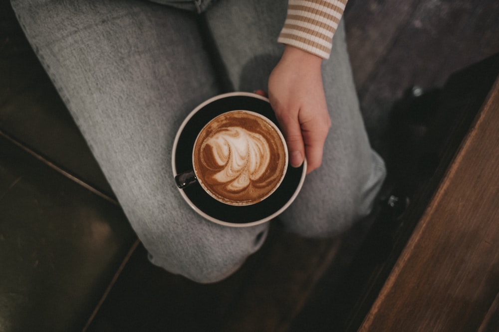 sitting person holding black saucer with white cappucino mug