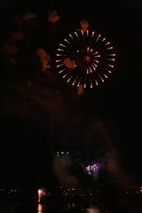 Fireworks bursting over the pond as festival-goers swim and relax nearby.