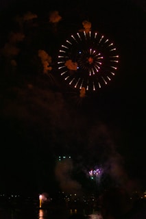 Fireworks bursting over the pond as festival-goers swim and relax nearby.
