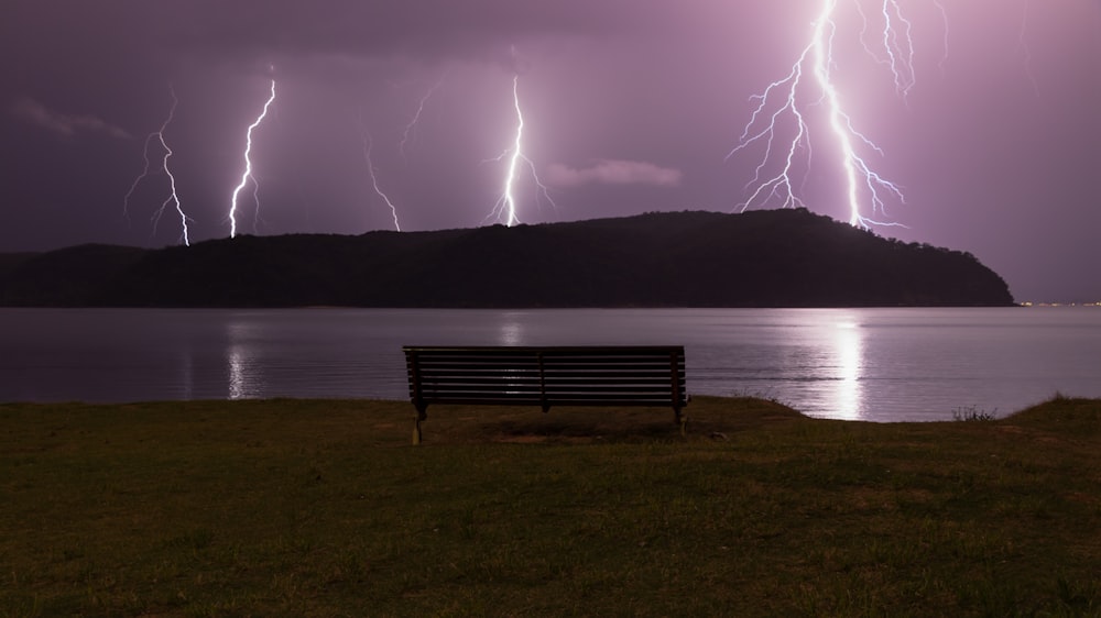 brown bench front of body of water with thunder storm