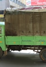 green and brown drop-side truck near gray building