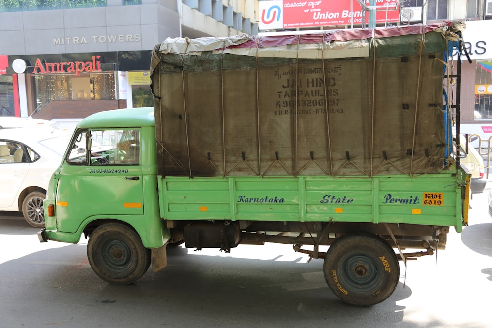 green and brown drop-side truck near gray building