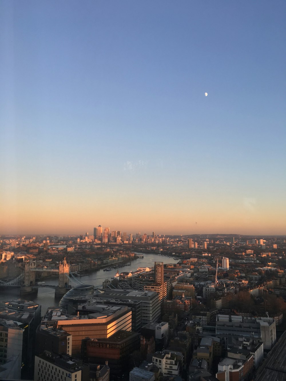 moon seen on blue and orange sunset sky over the city