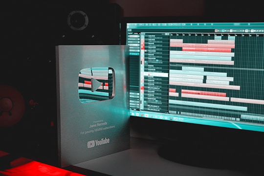 A YouTube Silver Play Button award is placed next to a computer monitor displaying music production software with various audio tracks and timelines.