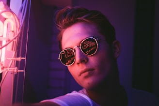 Retro-style sunglasses glowing under pink and purple neon lights.