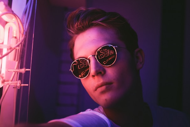 Retro-style sunglasses glowing under pink and purple neon lights.