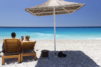 couple sits on sunlounger near open cottage at the beach