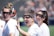 Three women with goggles stand closely together, wearing white sports shirts with logos on them. One woman waves toward the camera with a wide smile, adding a sense of camaraderie among them. The background is out of focus, possibly a sports field, indicating an outdoor setting.